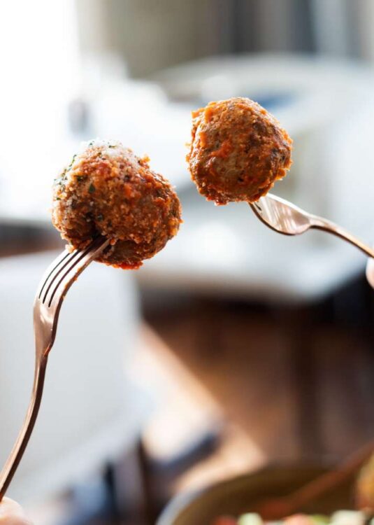 two people each holding up a fork piercing a meatball